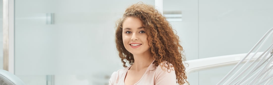 Long-Lasting Dental Fillings in Welland, ON | Welland Dental Centre Smiling young woman with curly hair sitting in a bright dental clinic