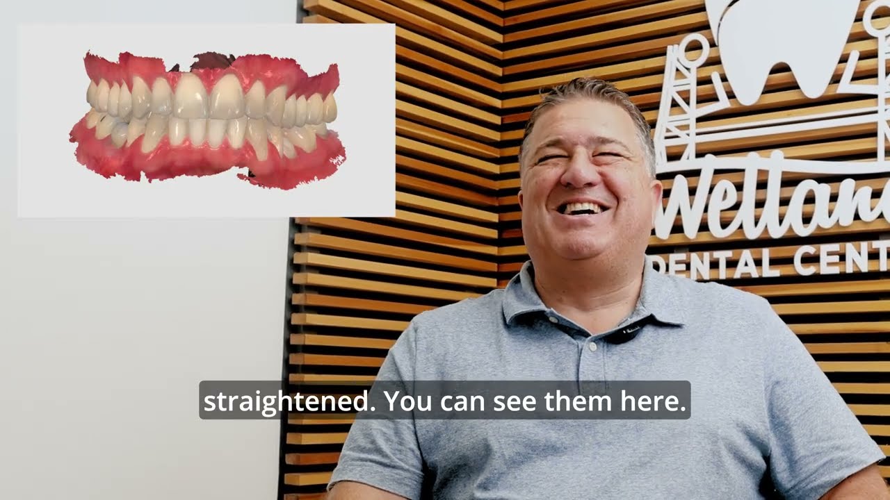 Patient smiling in front of the Welland Dental Centre logo wall with a 3D digital scan of his teeth beside him