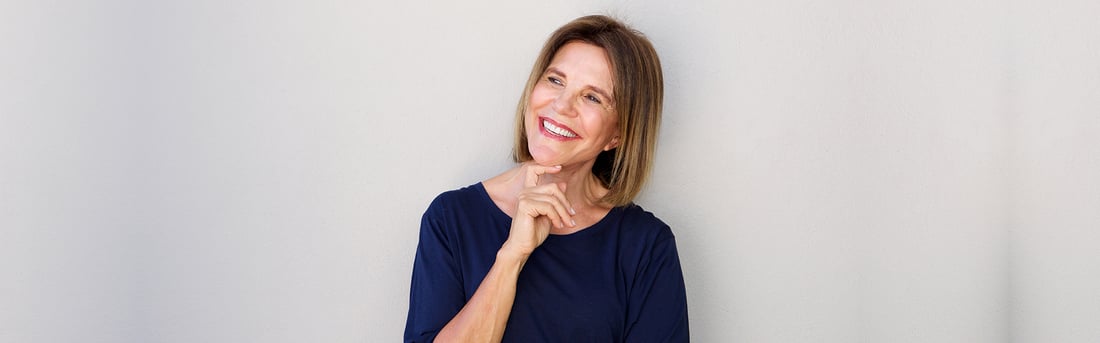 Smiling mature woman with a confident, restored smile leaning against a light wall