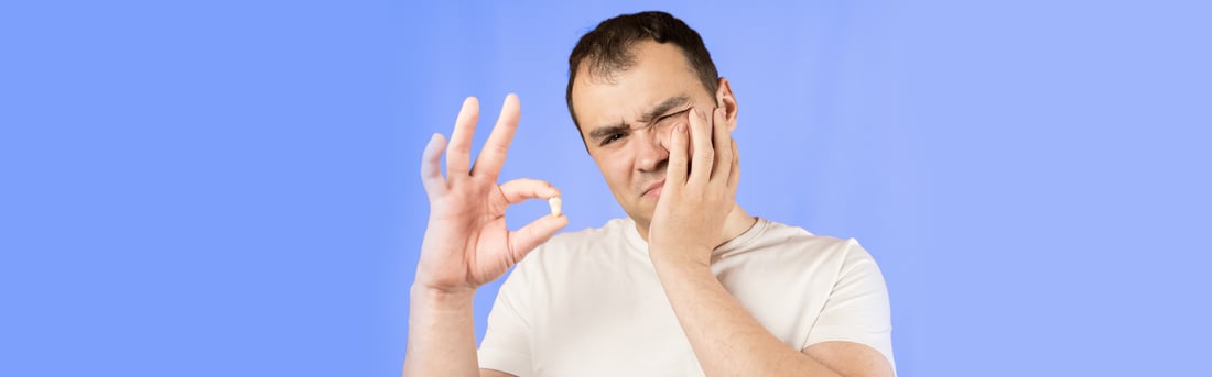 Man holding an extracted wisdom tooth while pressing his cheek in pain