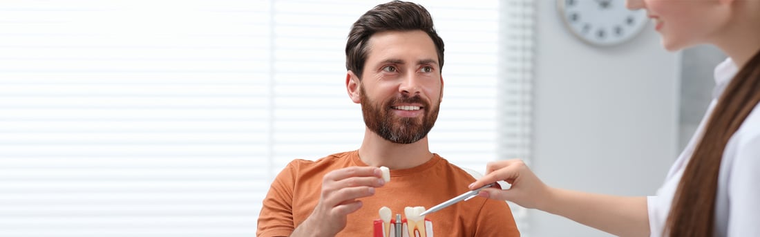 Dentist showing a smiling patient a dental implant model during a consultation